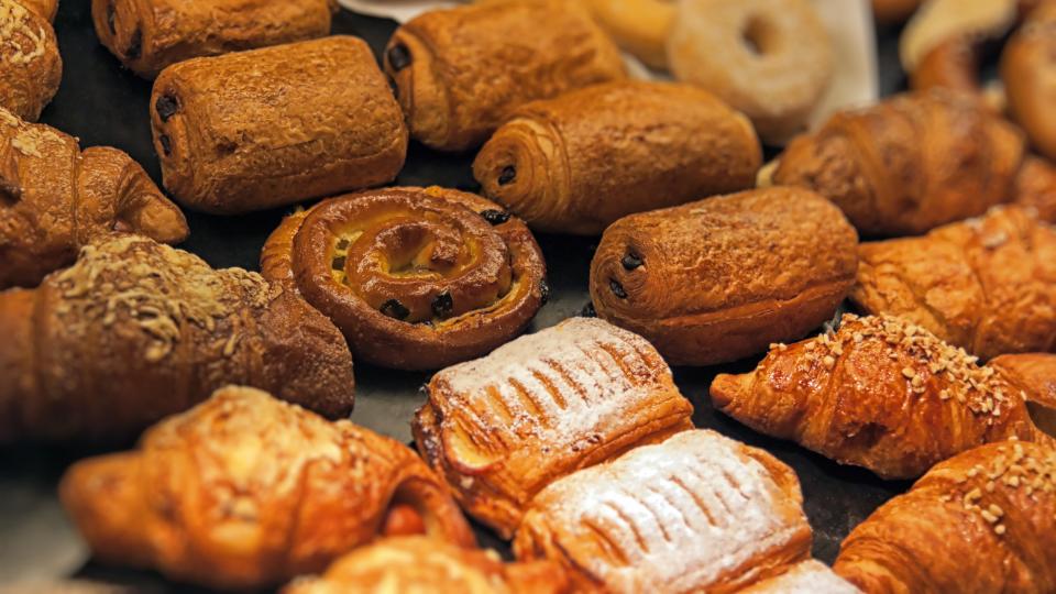 Photograph of bakery products. There are different pastries including pain au chocolats, almond croissants, apple turnovers, cheese croissants, wholewheat buns and sourdough rolls.