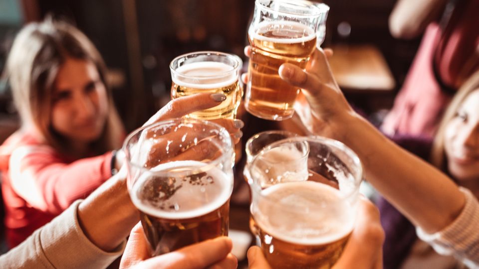 A photograph of people in a pub in England. They are smiling laughing and socialising and cheersing their glasses