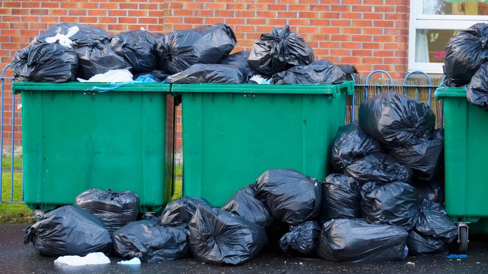 Black bin bags overflowing in 1100L green wheelie bins