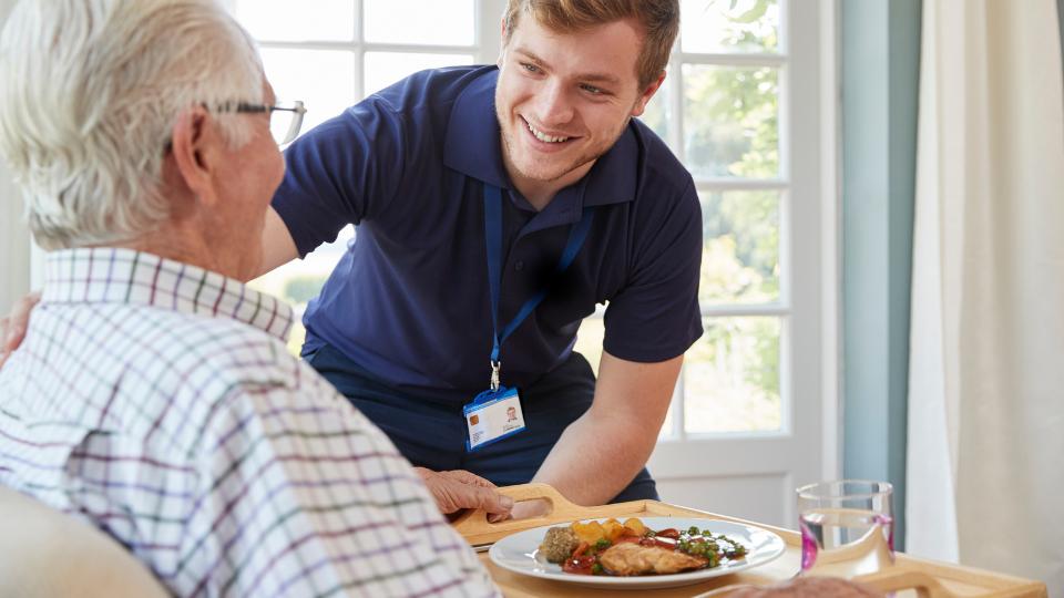 Care home staff giving food to eldery resident